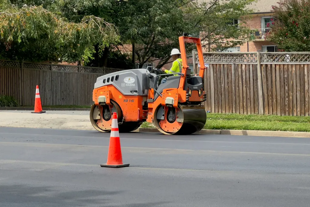 Roller compacting fresh asphalt beside traffic cones